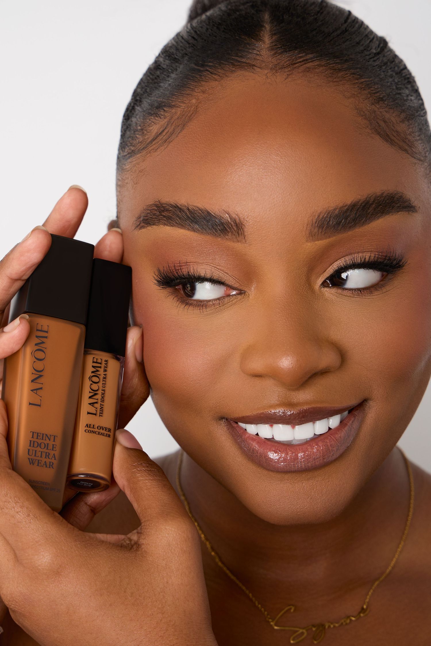 Beauty product advertisement showing foundation bottles held against face.