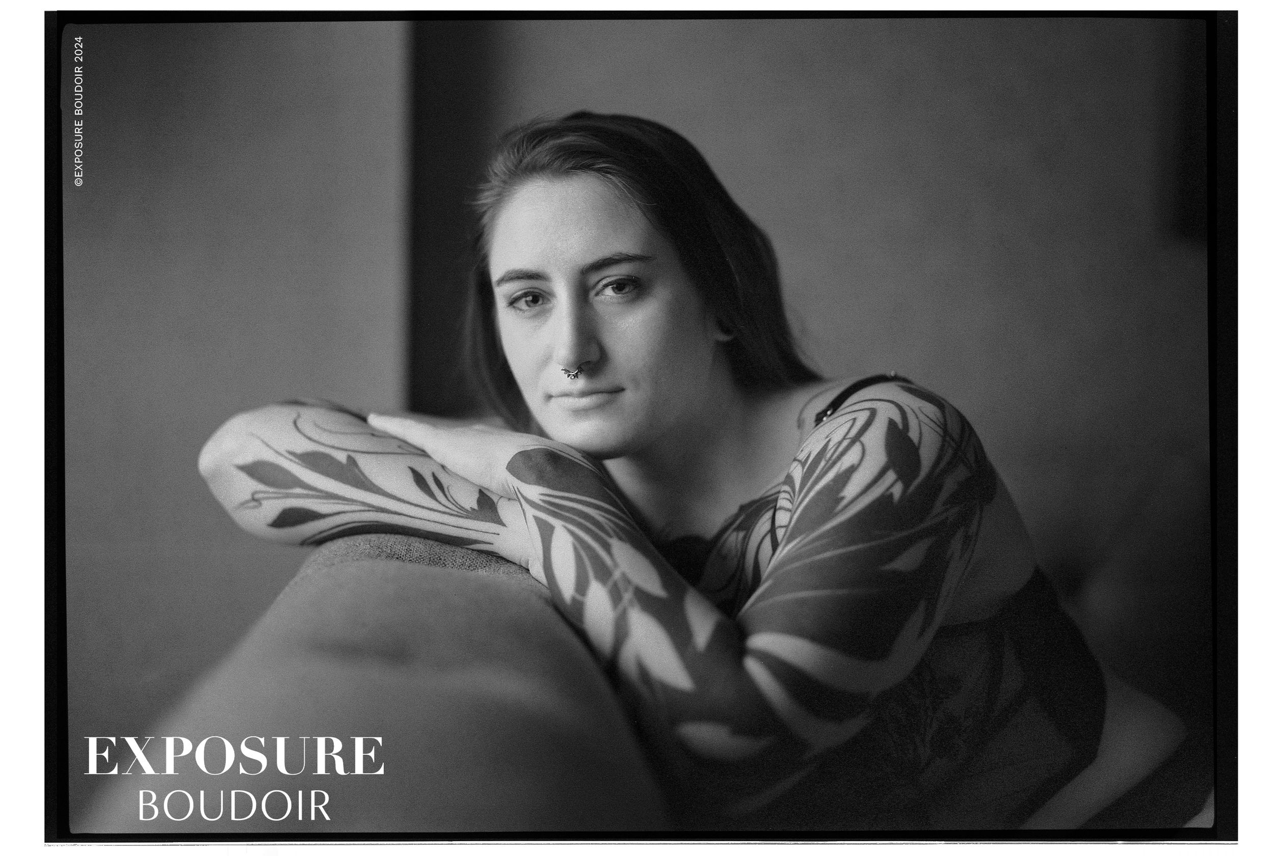 Black and white boudoir portrait showing figure with dramatic side lighting in flowing draped fabric against dark background.