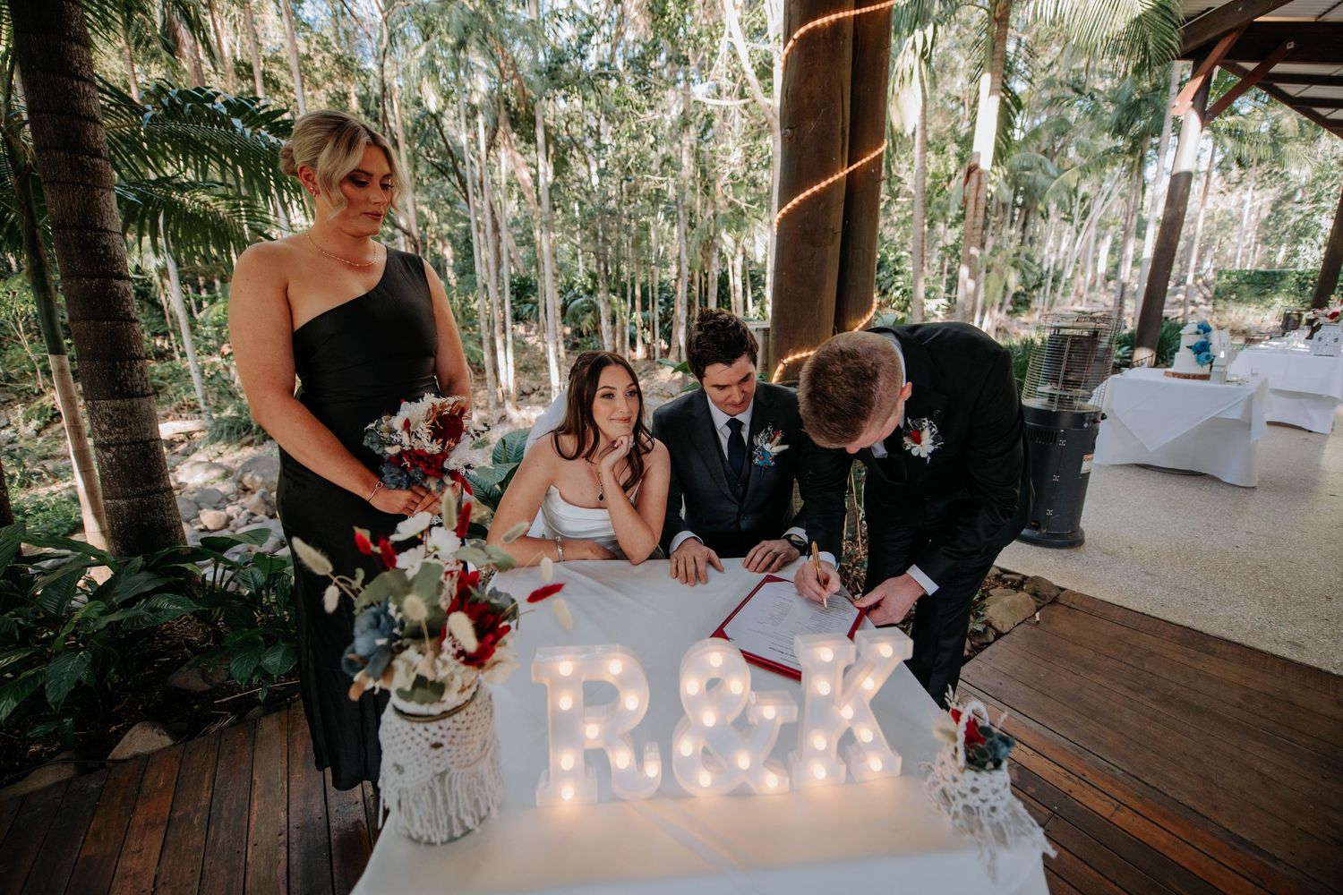 Wedding party gathered around illuminated sign during reception signing ceremony.