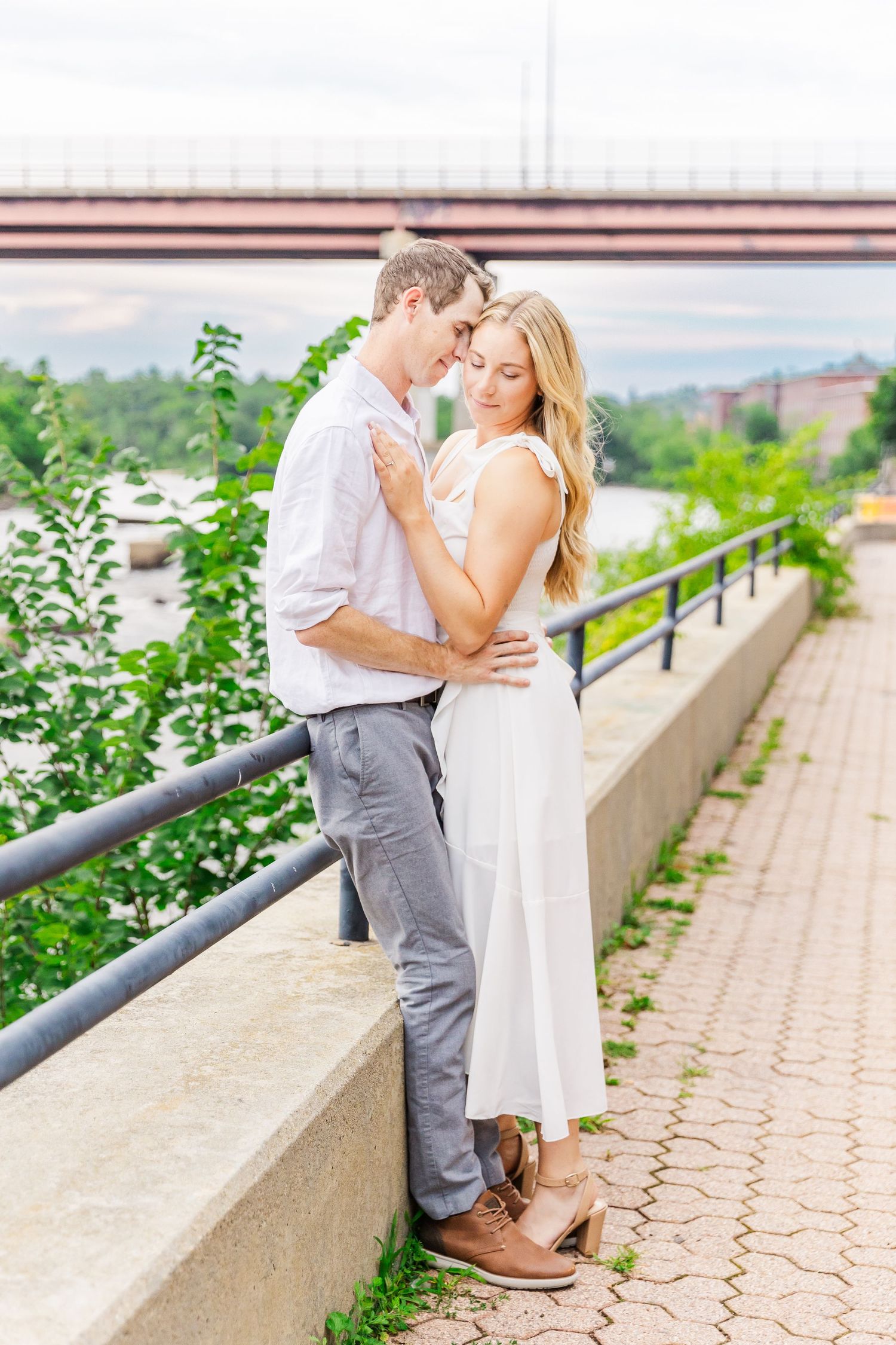 A tender moment captured between a couple on a paved walkway with city views in the background.