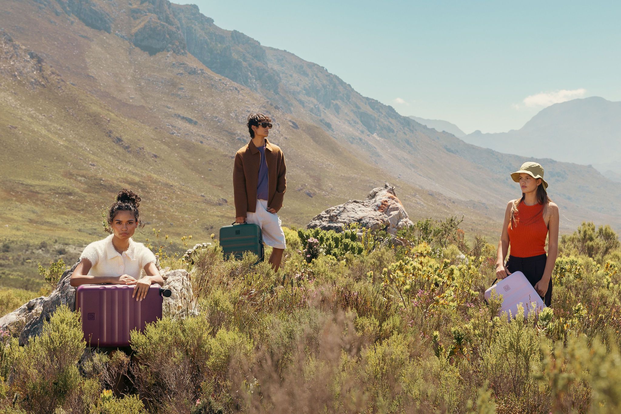 Group posing with colorful luggage in mountainous wildflower field.