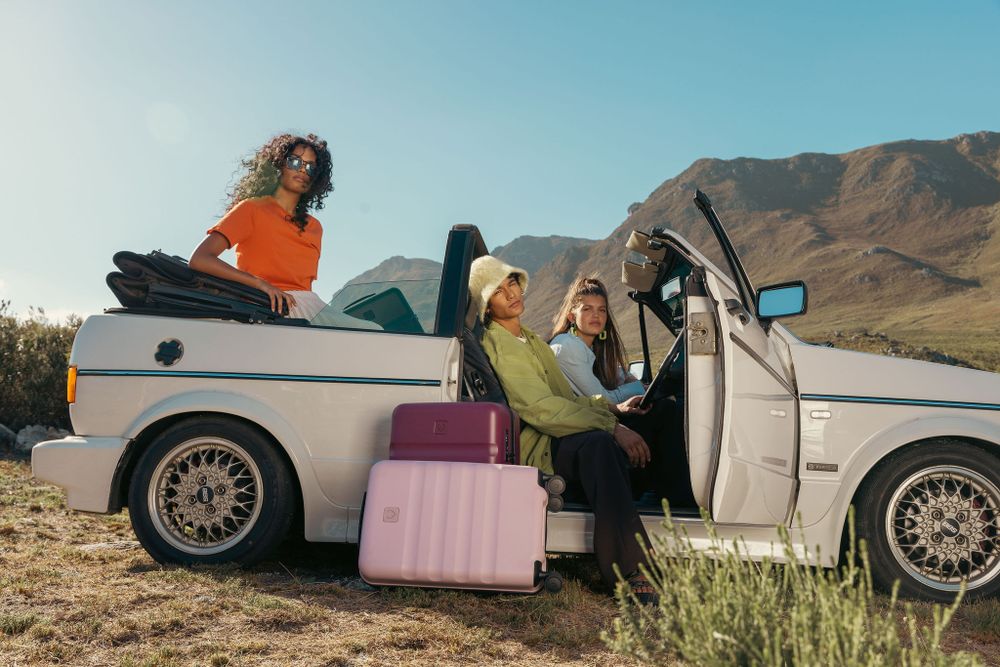 Group of friends with luggage gathered around classic white car in desert landscape.