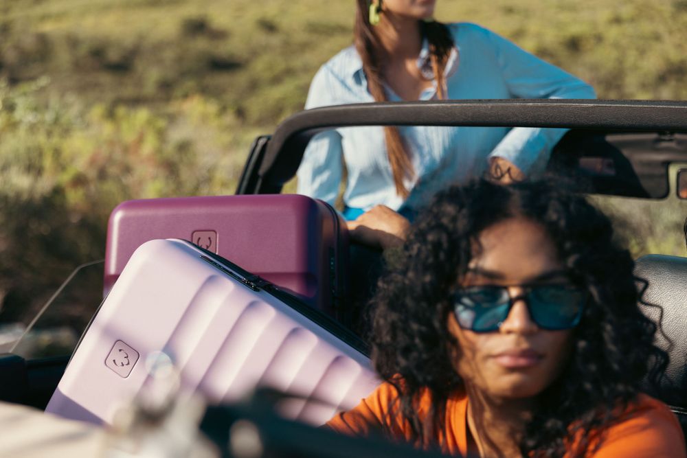 Travel scene with colorful luggage and vintage car against mountain backdrop.