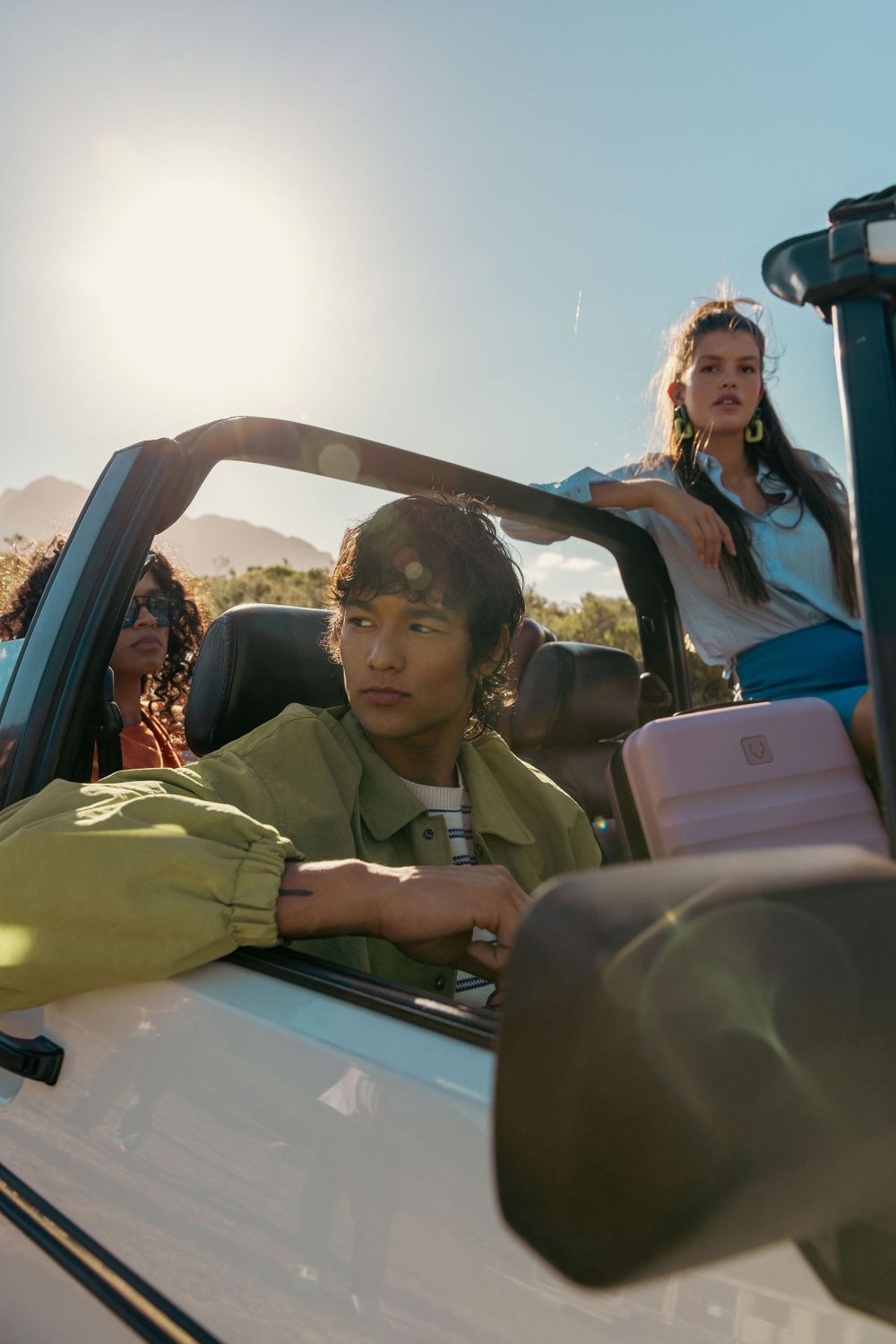 Friends in convertible car with luggage during sunny mountain adventure.