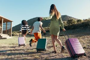 Group walking with colorful rolling luggage towards mountain cabin.