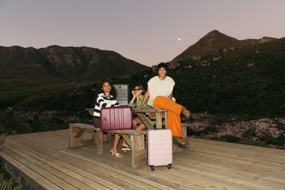 People relaxing on wooden deck furniture at sunset with mountains in background.