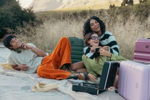 Friends relaxing on blanket with colorful luggage during sunny mountain picnic.