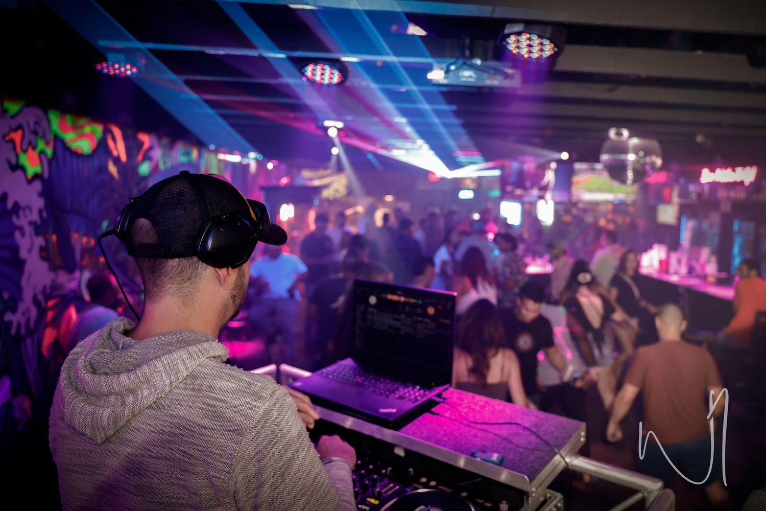 Crowded nightclub interior illuminated with purple and blue lighting effects.