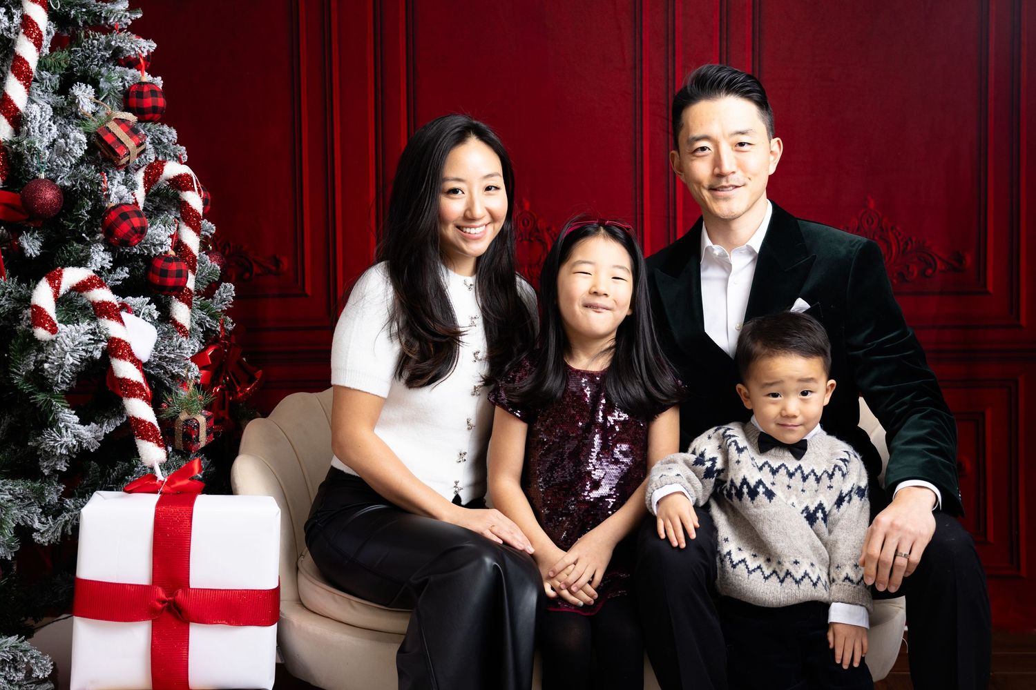 Family holiday portrait with decorated Christmas trees and wrapped presents in studio.