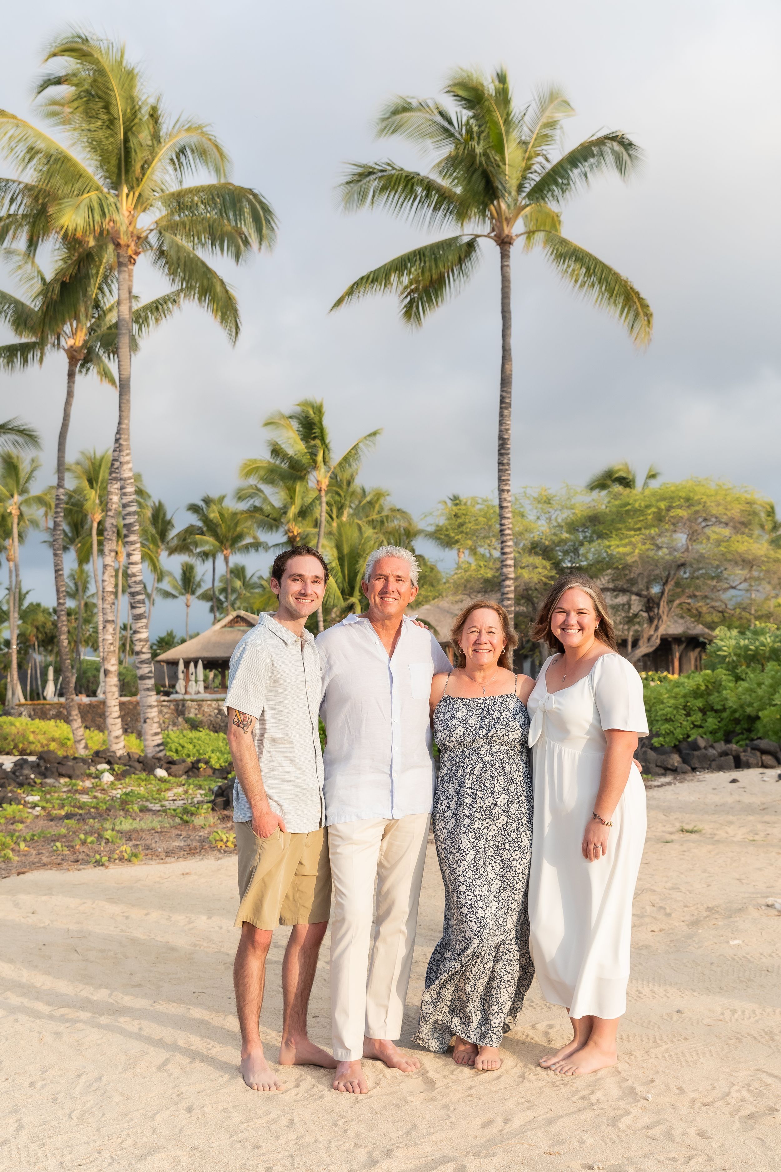A family stands together on a tropical beach with palm trees and ocean views in Hawaii during golden hour.