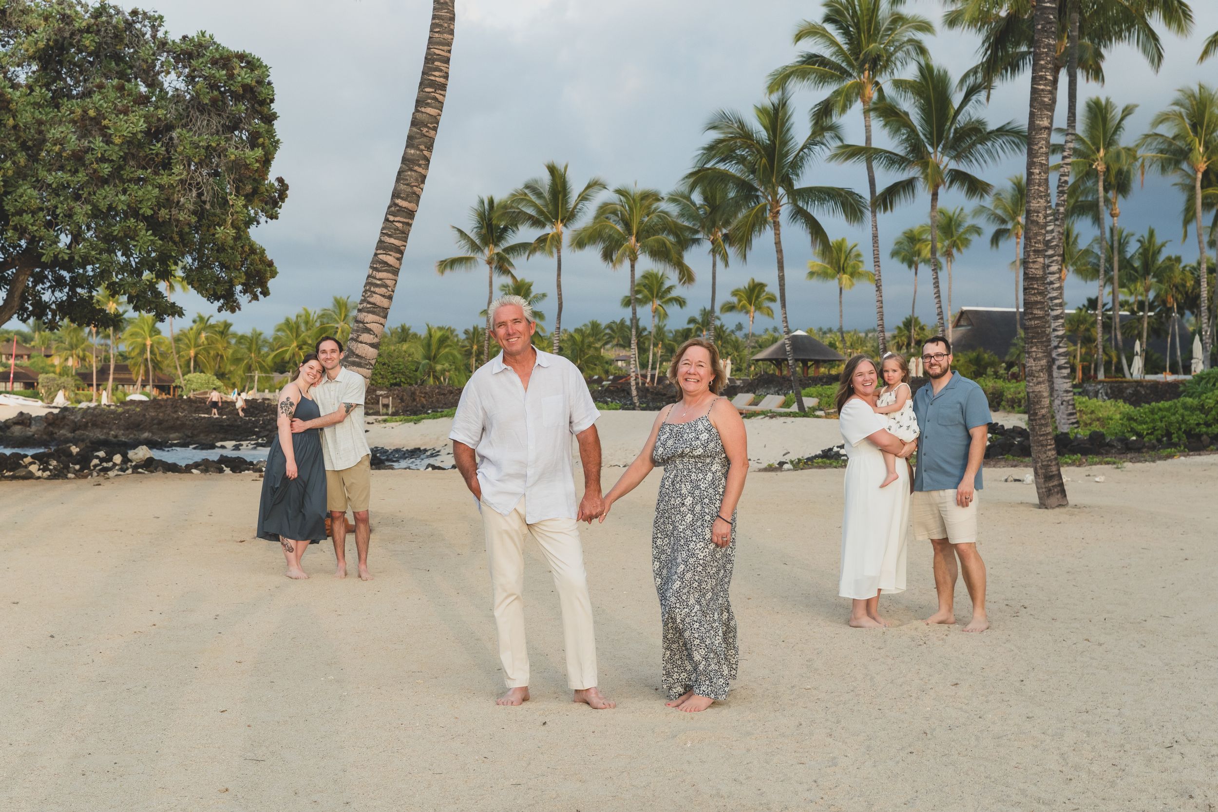 A group enjoys a stroll along a scenic Hawaiian beach with palm trees and lava rock walls on a sunny day.