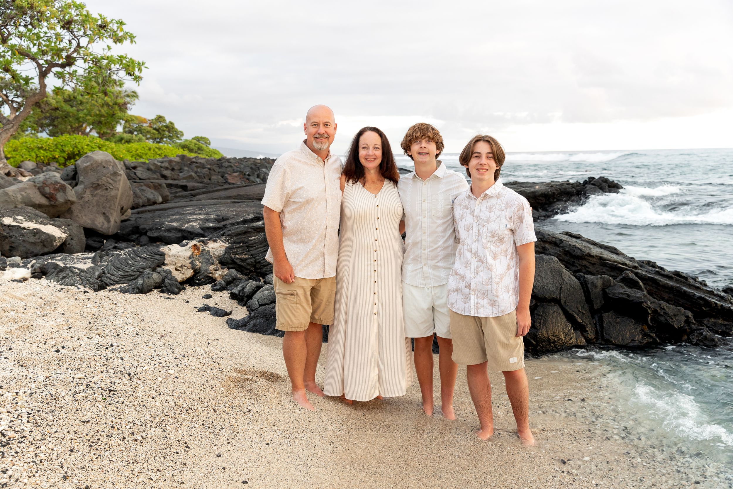 A group poses for a beach photo on white sand with black volcanic rocks and ocean waves behind them.