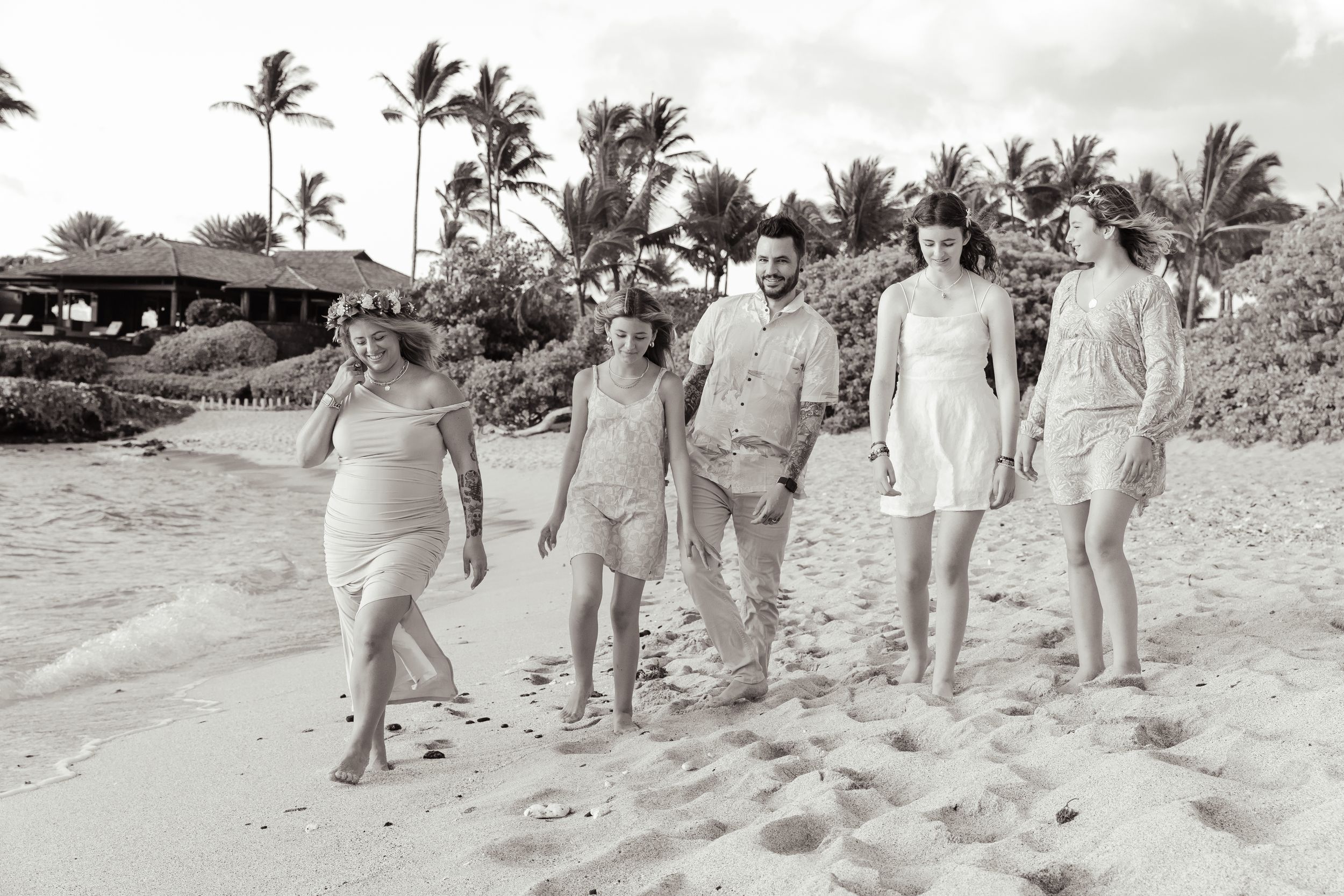A group enjoying a casual stroll along a tropical beach with palm trees in black and white.