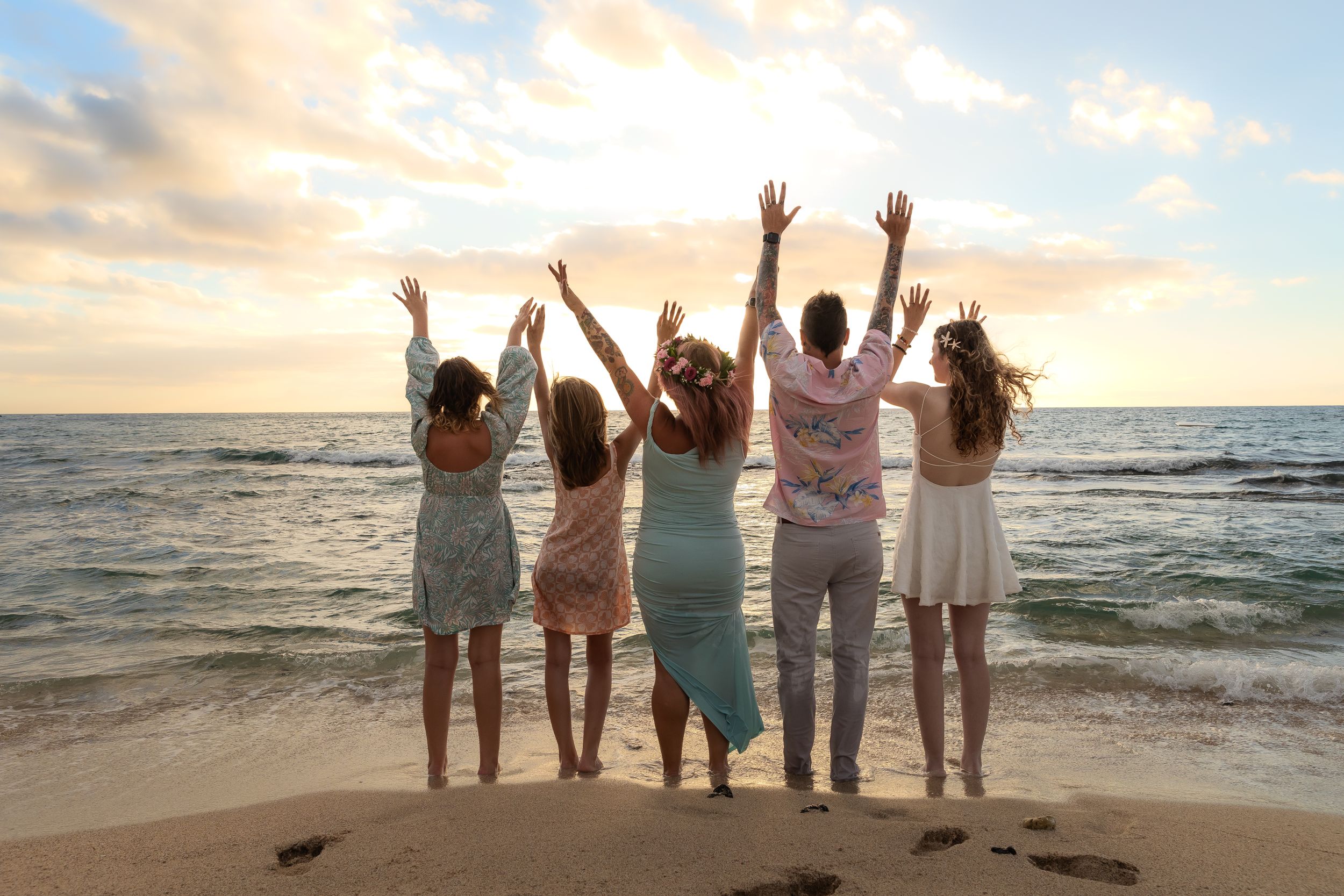 Friends with raised arms celebrating together on a beach at sunset.