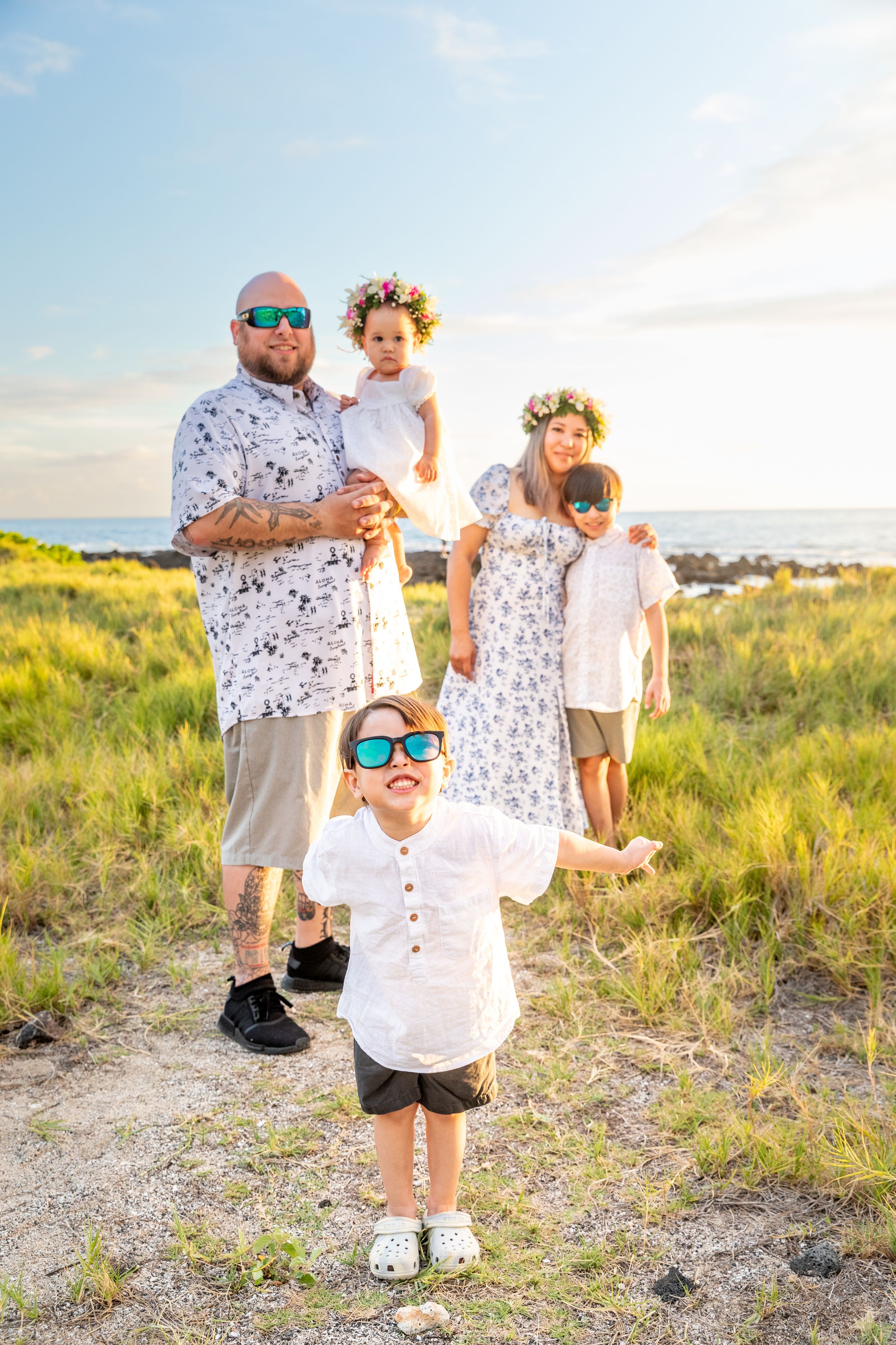 Family in coordinated outfits poses on grassy coastal terrain at sunset.