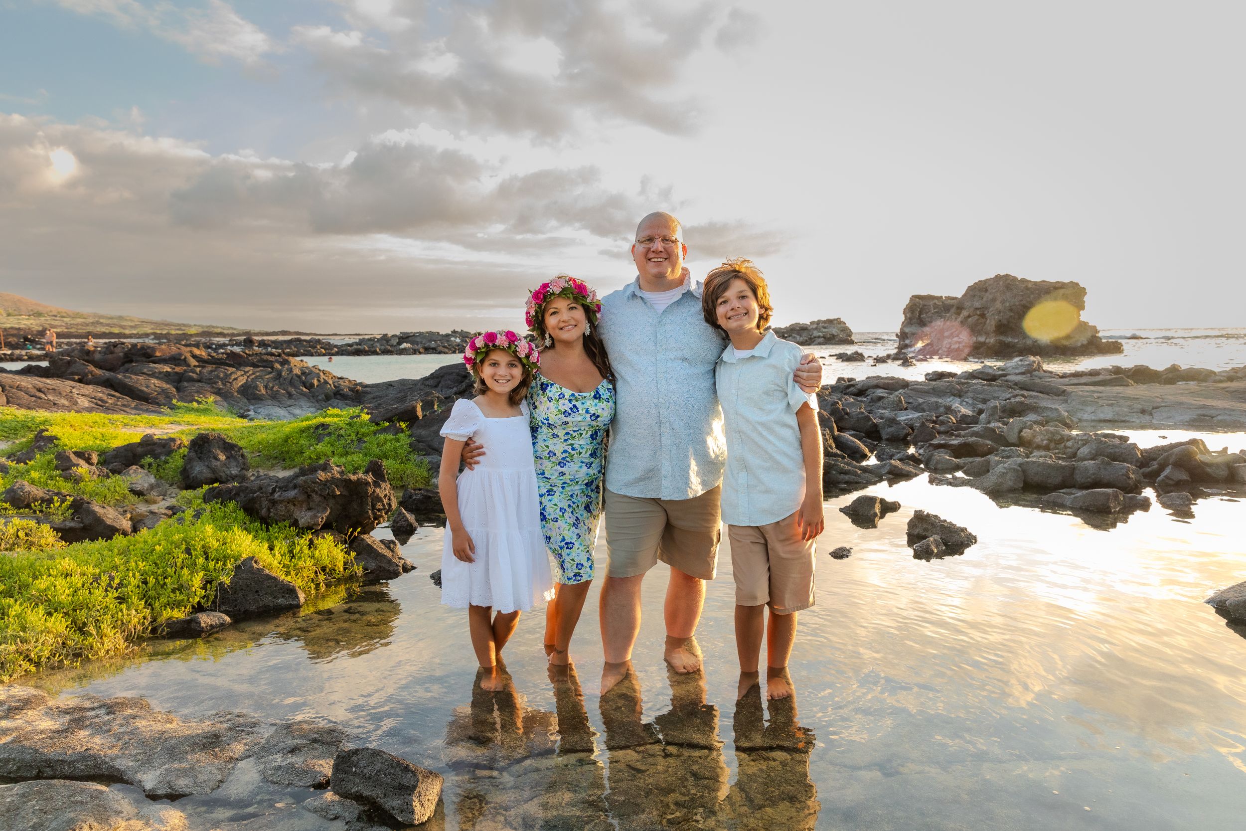 A family stands together on rocky coastal tide pools during golden hour in Hawaii.