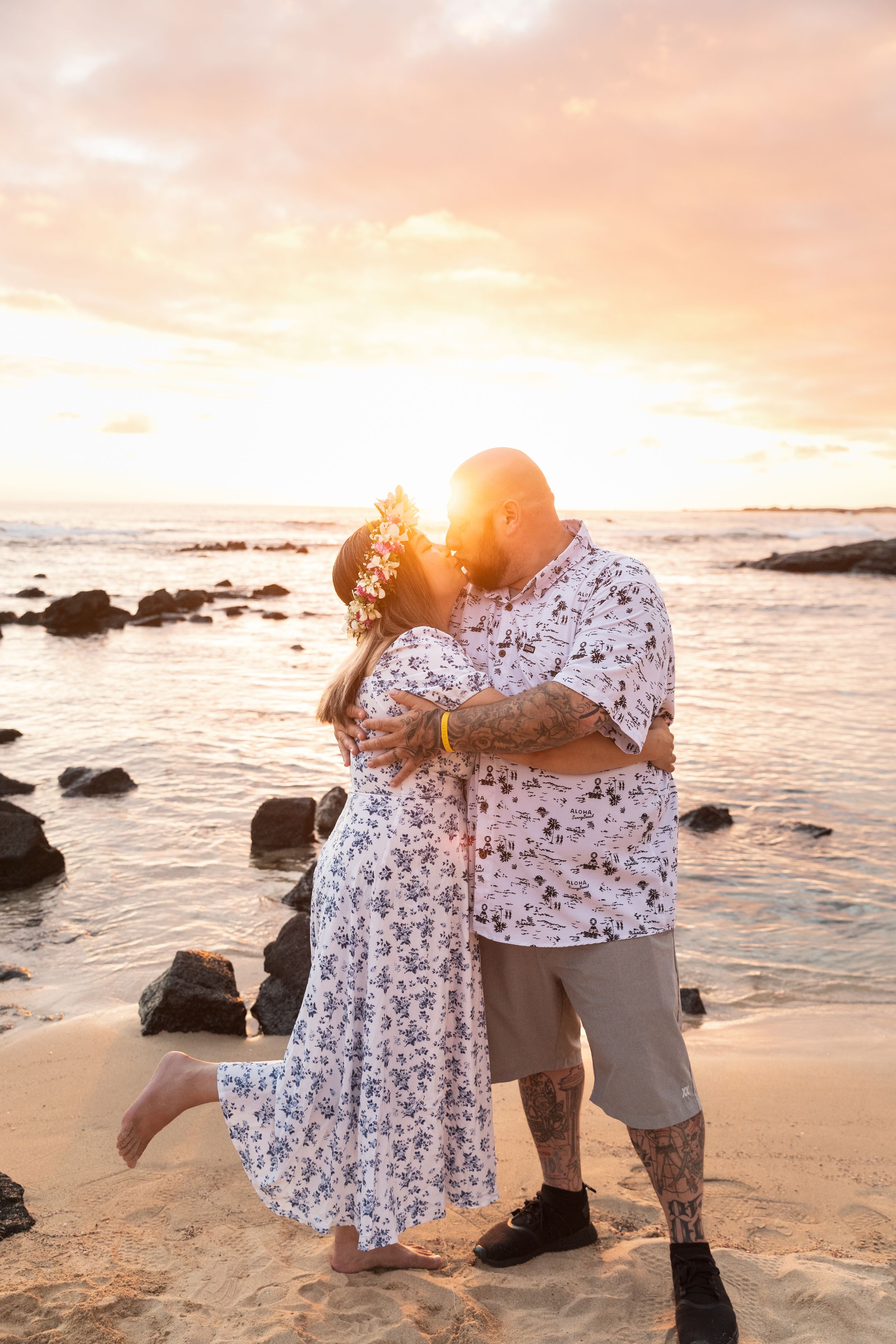 Couple in coordinating outfits sharing an intimate moment on beach at sunset.