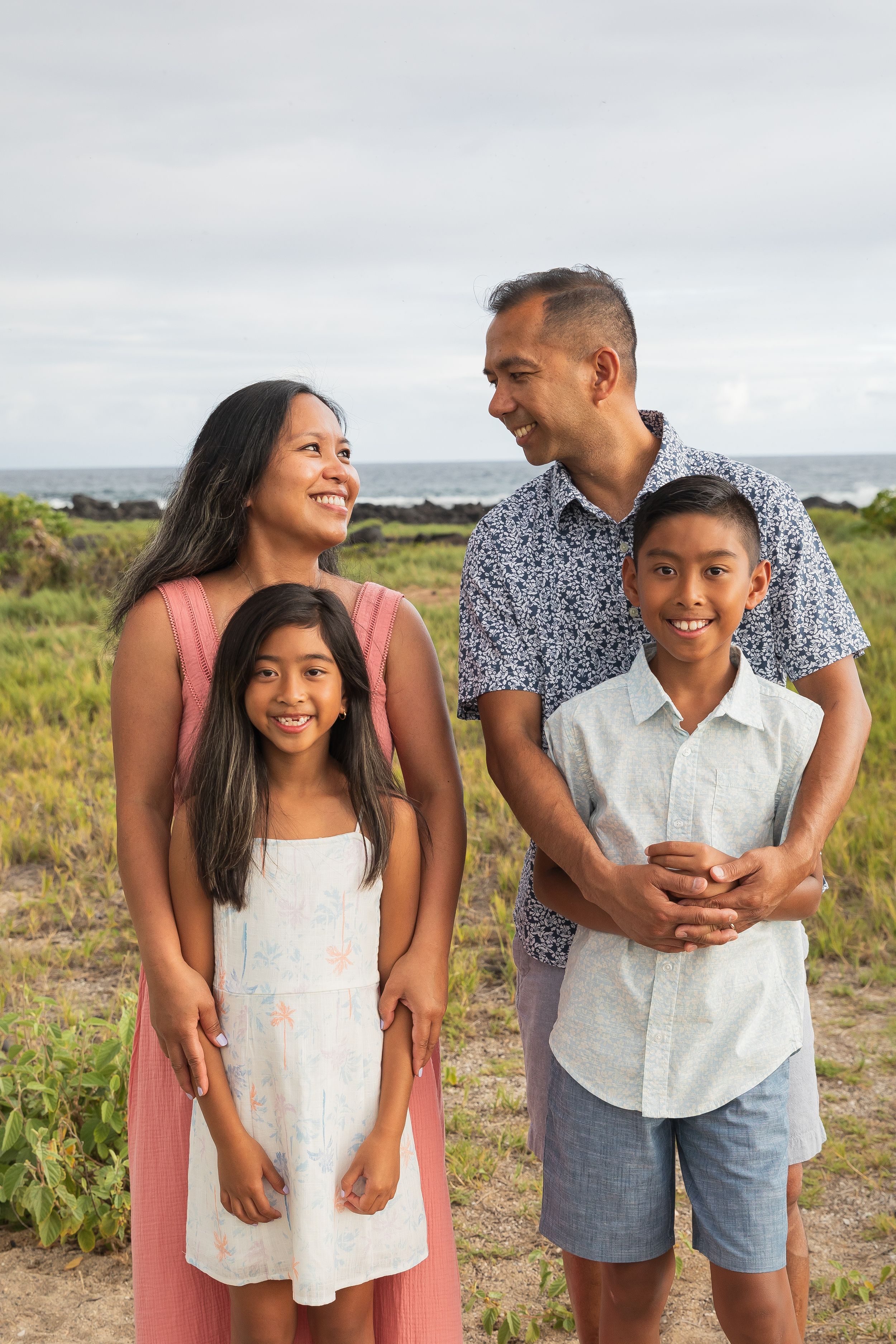 A family of four poses together on a coastal cliff with the ocean in the background.