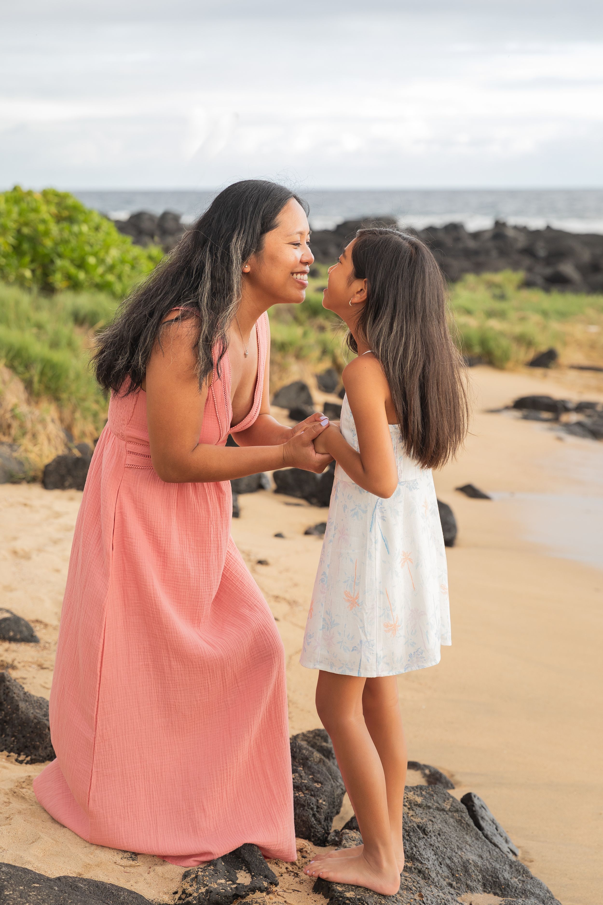 Two people share a loving moment on a beach with volcanic rocks and ocean in the background.