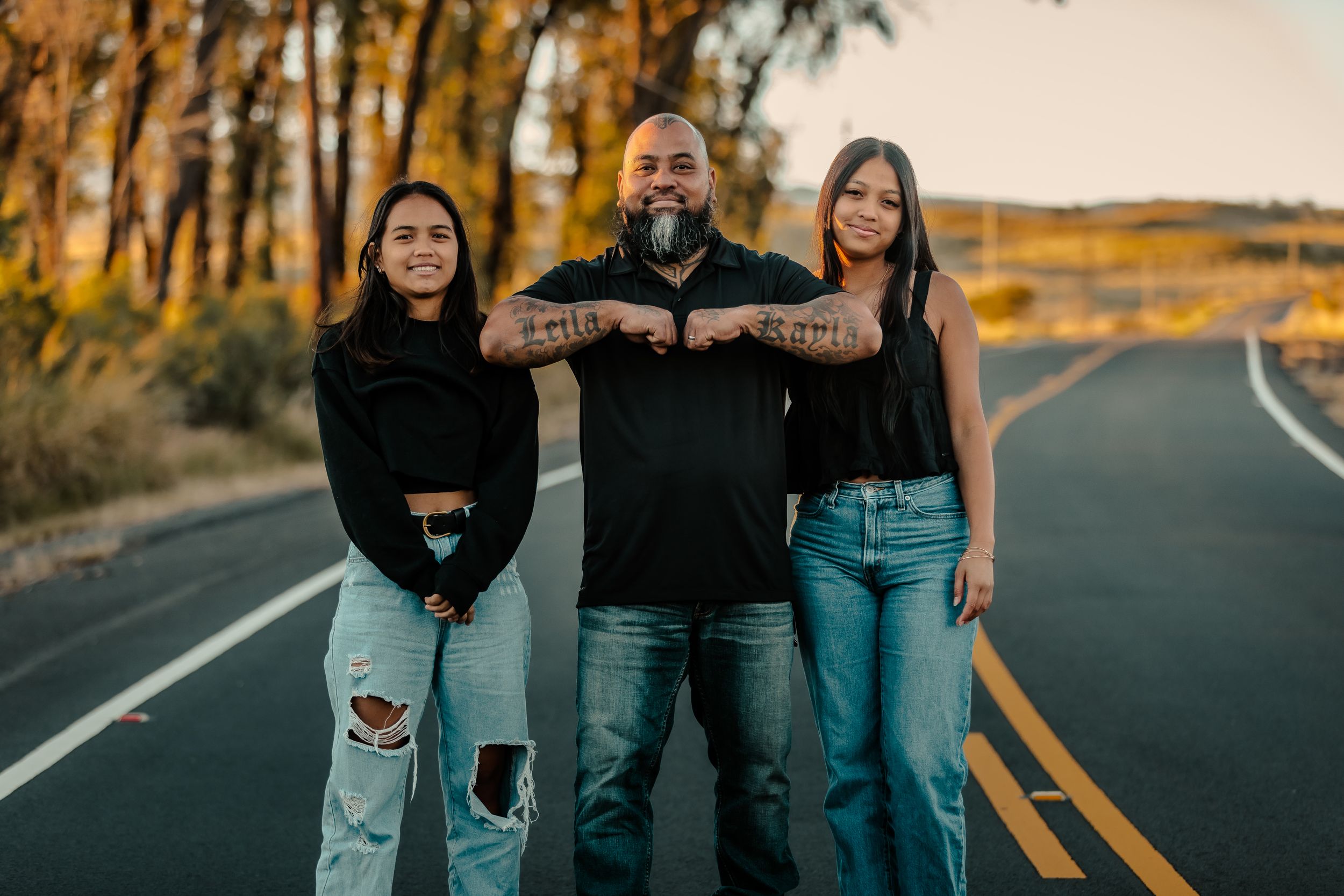 Three people pose casually on a rural road at sunset.