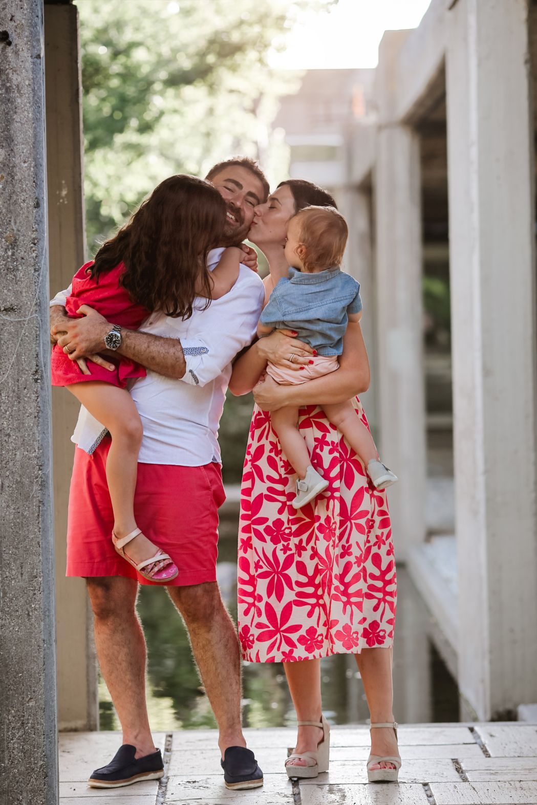 A tender family moment shared between parents and children in a sunlit outdoor walkway.