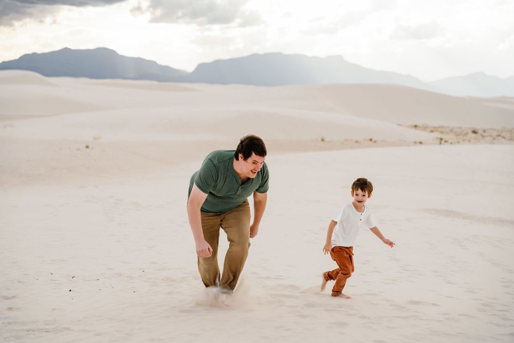 Two figures playfully running across white sand dunes with mountains in the background.