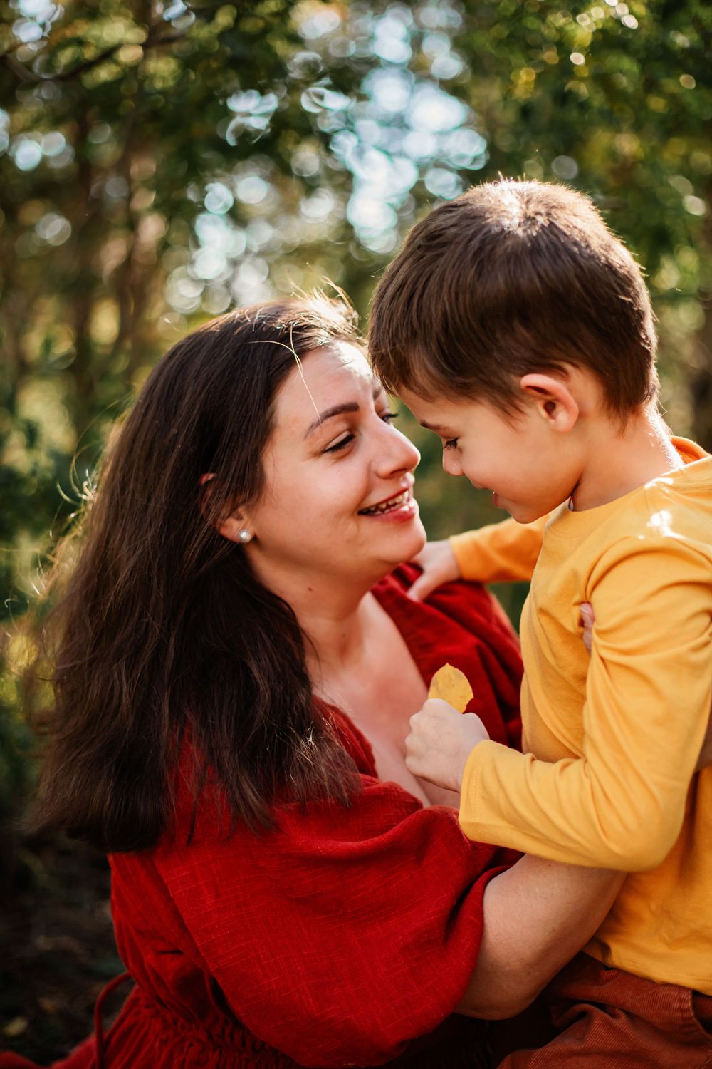 Tender moment captured outdoors with autumn trees in background.