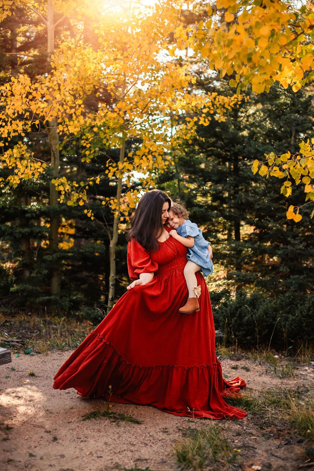Red dress flows dramatically against golden autumn trees in sunlit forest scene.