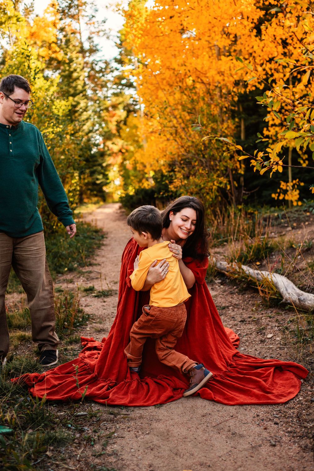 Family walking together on forest path surrounded by vibrant fall foliage.