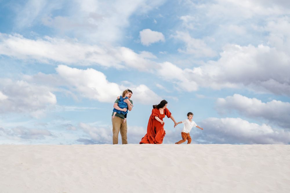 Three silhouettes playing and running on sand dunes against a bright blue sky.