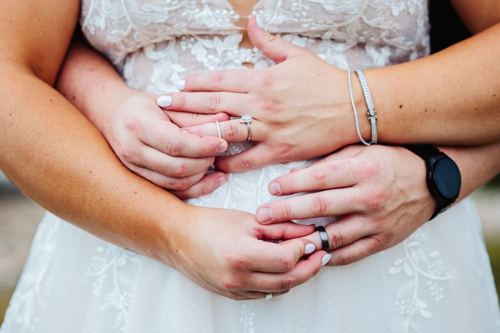 Close-up of hands with wedding rings and bracelet on white lace dress.