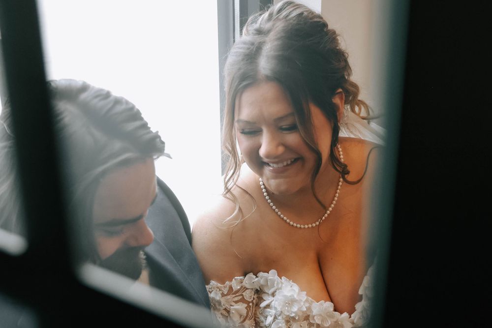 A candid moment between newlyweds sharing laughter near a window.