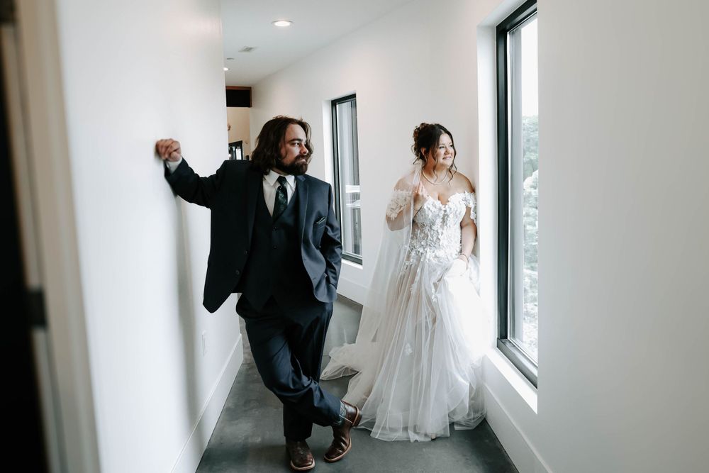 Couple walking playfully down bright hallway, bride in flowing white gown and groom in dark suit.