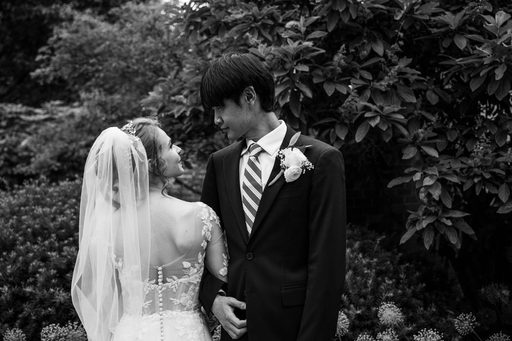 A bride and groom share an intimate black and white moment together in a garden setting.