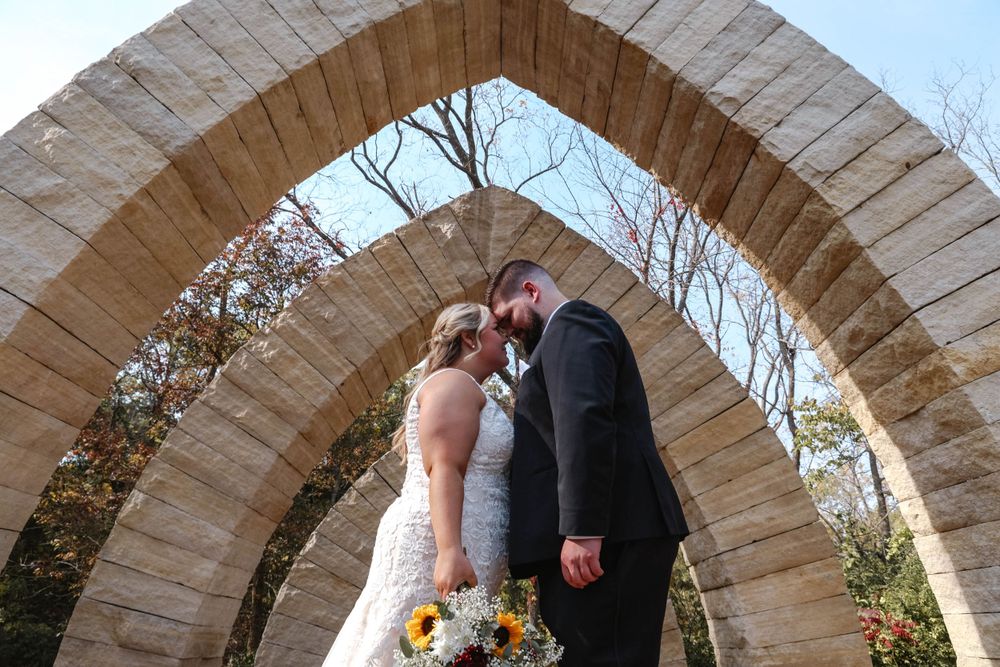Romantic wedding photo of couple sharing an intimate moment under a stone archway.