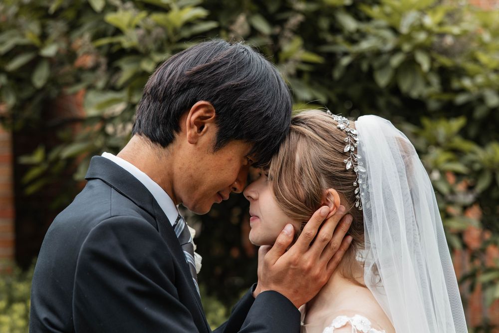 A tender moment between newlyweds as they share an intimate embrace outdoors, with the bride wearing a white veil.