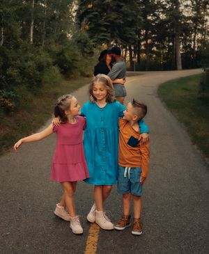 Three children in colorful outfits playing on a forest path at sunset.