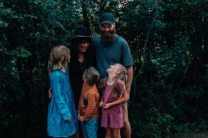 Family of five poses together against lush green forest backdrop wearing casual clothing.
