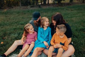 A candid outdoor family photo showing five people sitting together on a sunny day in a grassy field.