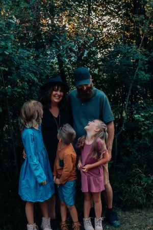 Family group portrait in wooded setting at sunset wearing casual clothing.