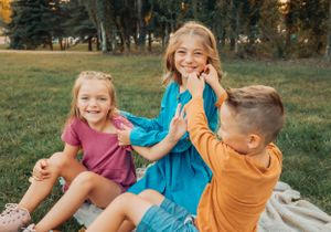 Three children in colorful clothing sitting and playing together outdoors.
