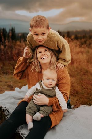 An autumn outdoor portrait shows a cozy family moment with warm sweaters against a mountain backdrop.