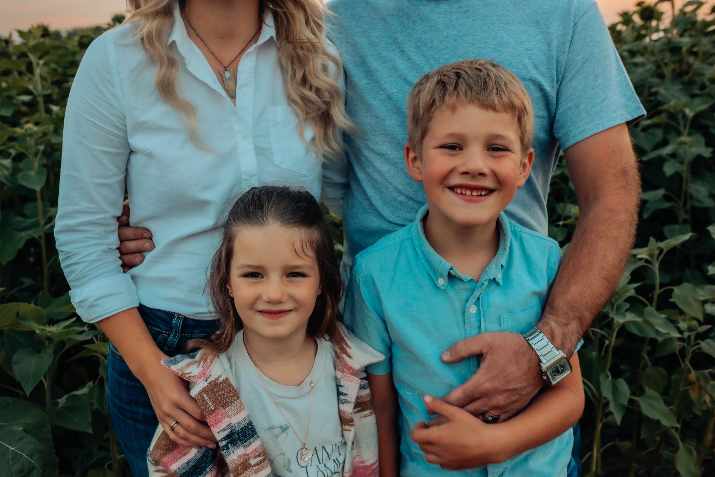 Family wearing coordinated turquoise and white outfits poses together against green foliage backdrop.