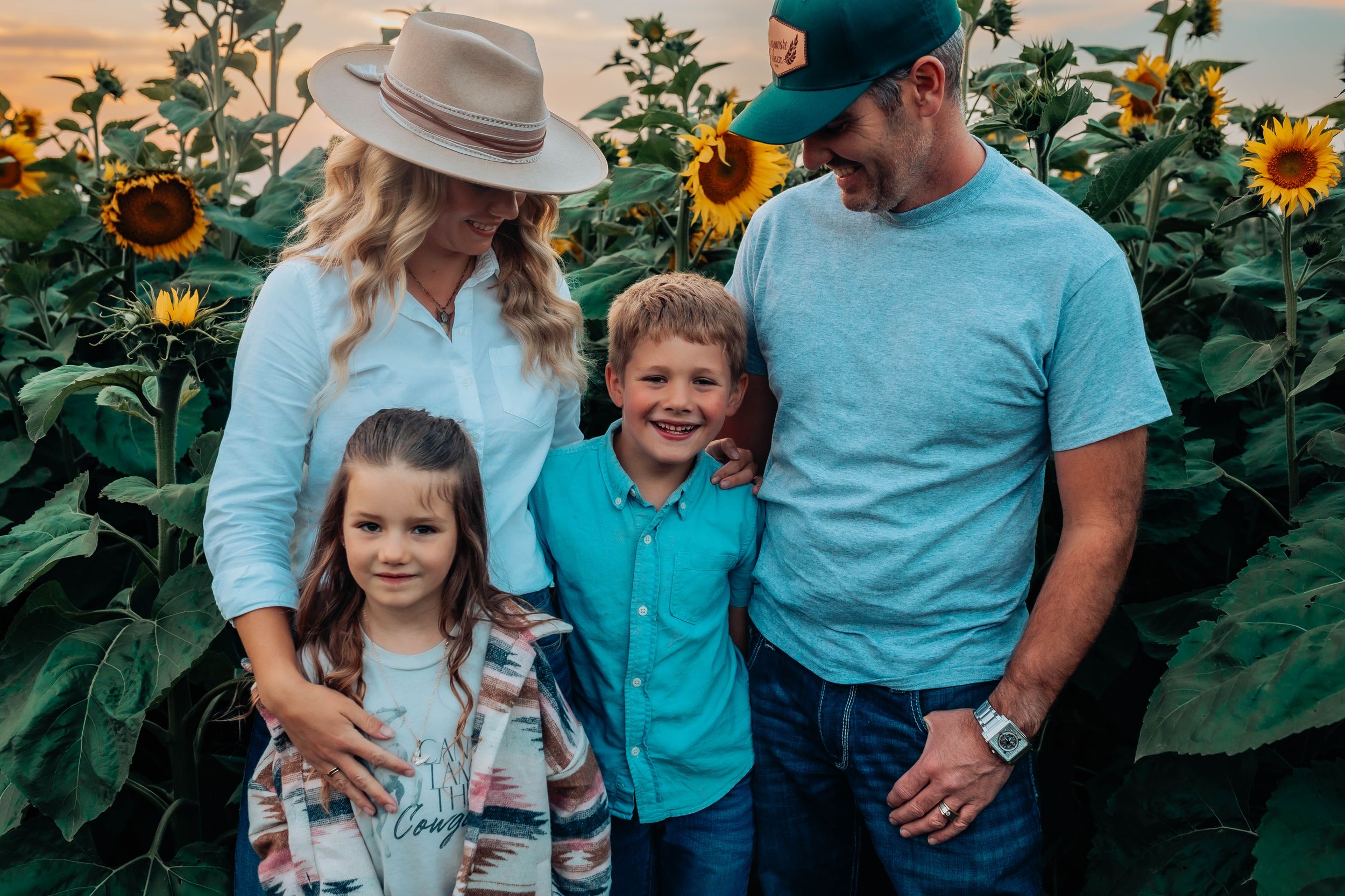 Casual family portrait among blooming sunflowers with rustic truck backdrop.