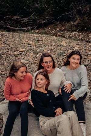 Four friends in cozy sweaters share genuine smiles while sitting together on rocky ground.