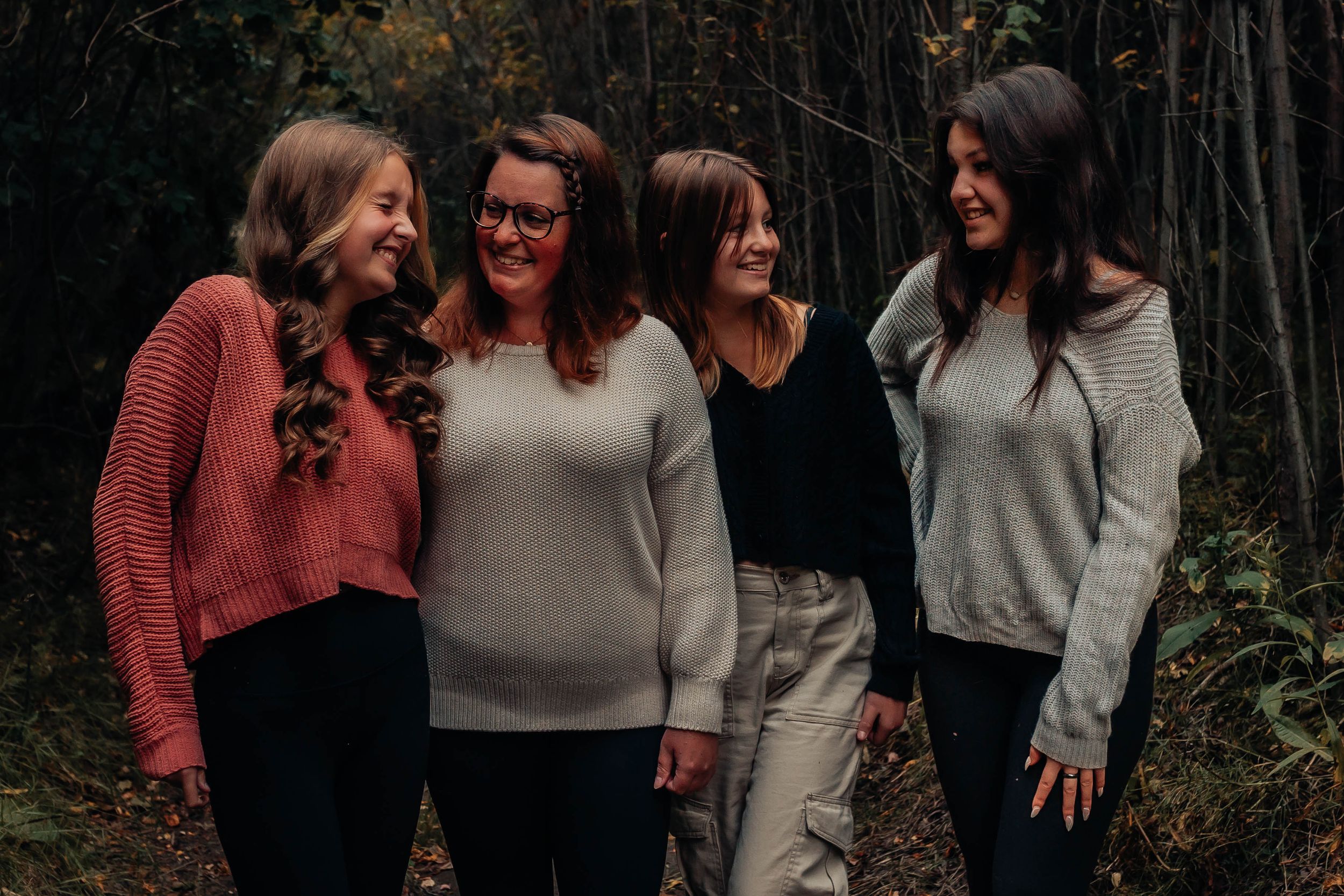 Four friends in cozy sweaters share laughs together in wooded setting.