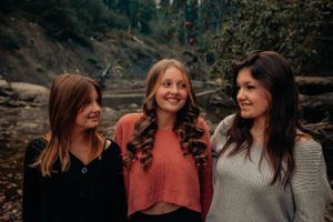 Three friends in warm sweaters share genuine laughter outdoors.