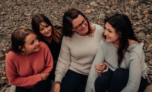 Four friends in casual sweaters share authentic moment of laughter on rocky ground.