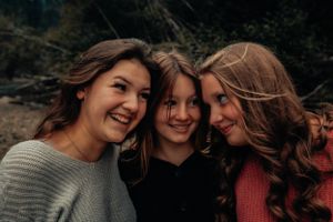 Three friends share intimate moment of joy while embracing outdoors.