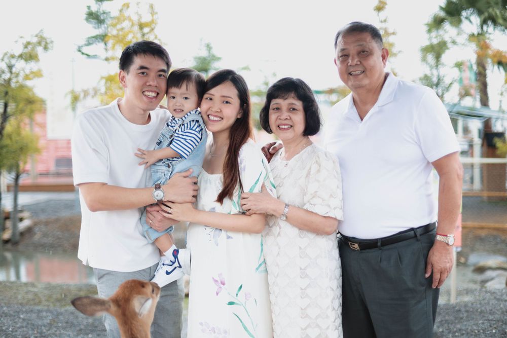 Asian multigenerational family of five smiling together outdoors near a pond.